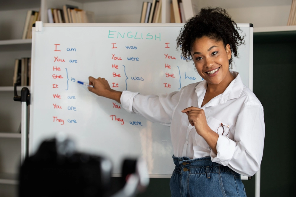 A professional English teacher in a bright Madrid classroom, smiling and pointing to a lesson on a whiteboard, demonstrating active student engagement.