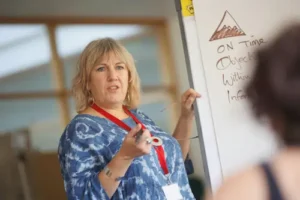 A professional teacher pointing to an English lesson on a whiteboard while smiling at students in a bright Madrid classroom.