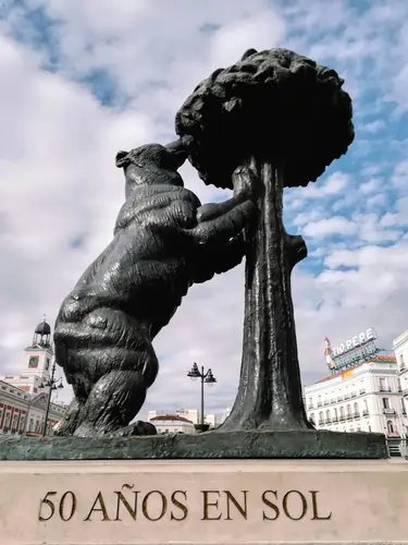 The bronze statue of the Bear and the Strawberry Tree in Puerta del Sol, Madrid, under a clear blue sky.