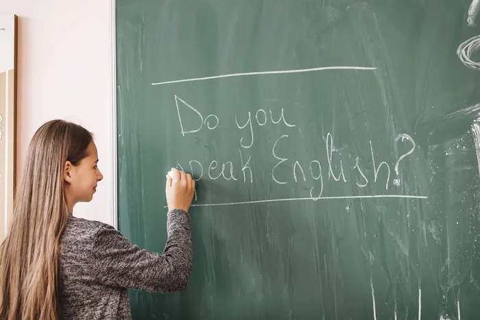 A young student writing "Do you speak English?" in chalk on a green blackboard during an English lesson in Madrid.