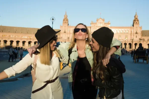 Three teachers laughing and hugging in a sunny Spanish plaza, showcasing teaching English and community Madrid bonds.