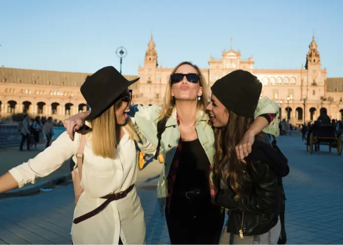 Three teachers laughing and hugging in a sunny Spanish plaza, showcasing teaching English and community Madrid bonds.