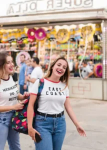 wo TEFL teachers laughing and holding pink ice cream cones in front of a traditional Spanish "Helados" stand, showcasing the social teaching English in Madrid lifestyle.