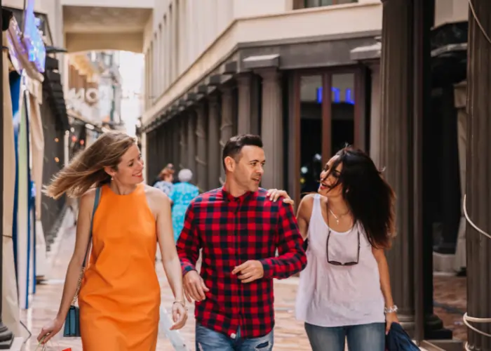 Three friends walking together through a classic Madrid street with columns, laughing and talking in a relaxed social setting.