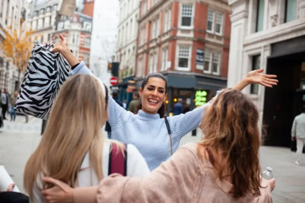 Three young women smiling and greeting each other with open arms on a Madrid city street, representing a warm reunion and friendship.