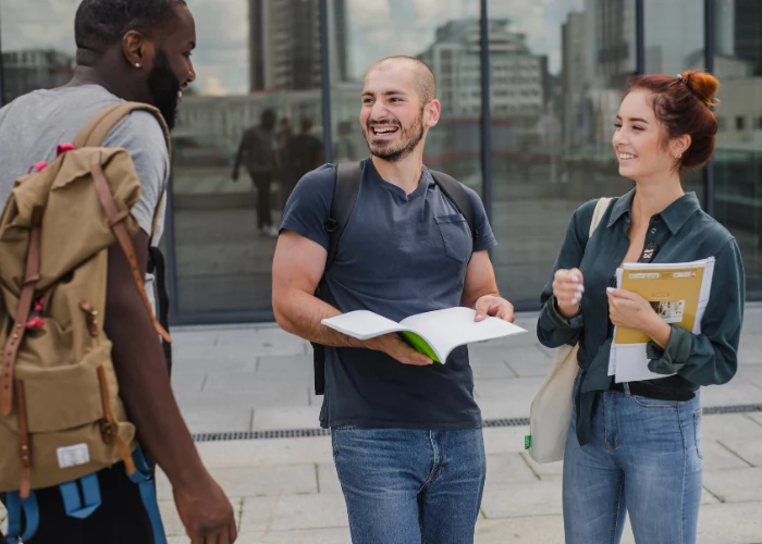 A group of three professionals standing together in a modern office; two women and one man are smiling warmly while holding notebooks and business documents.