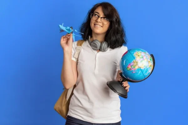 A young woman holding a small globe and a toy airplane, looking upward with a hopeful expression as if dreaming of international travel and a new life abroad.